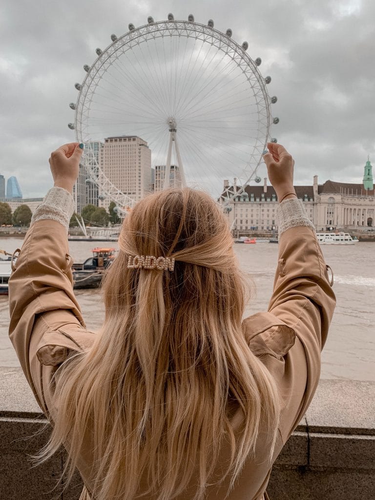 Jeune fille de dos à Londres, faisant mine de tenir London Eye dans ses mains 