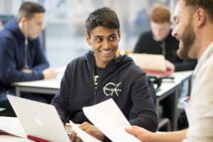 Des étudiants échangeant en cours avec ordinateur et feuilles de cours